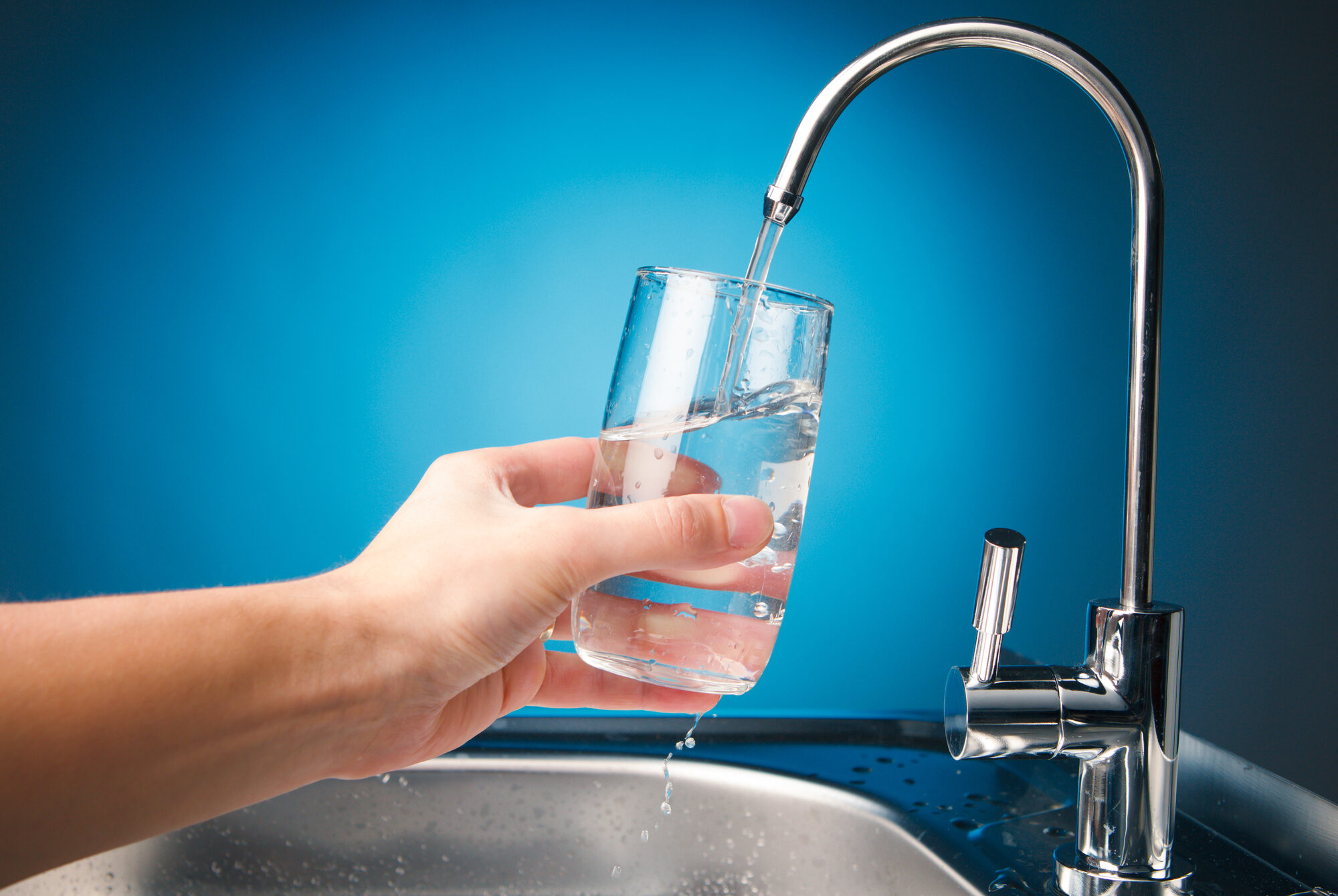 hand pouring a glass of water from filter tap, blue background